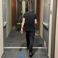 a man walking down a hallway in a black hat